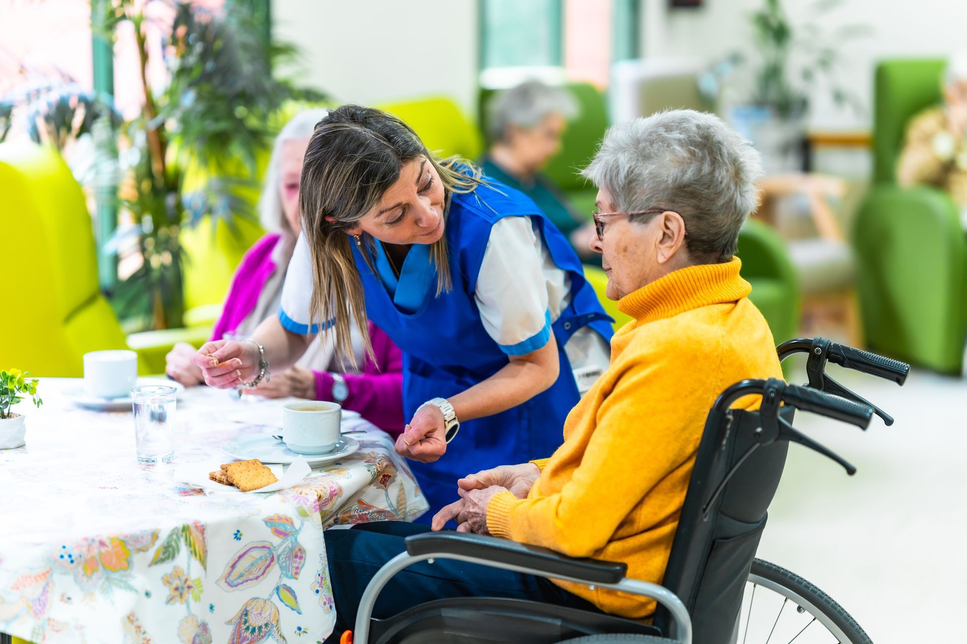 Caregiver serving tea to a seated older adult in a bright nursing home dining area Caregiver serving tea to a seated older adult in a bright nursing home dining area