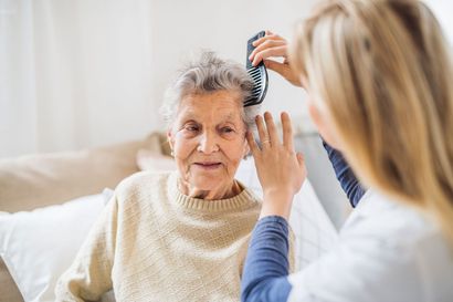 Hair being combed during a home care visit; elderly woman sits on a couch, looking forward. Hair being combed during a home care visit; elderly woman sits on a couch, looking forward.