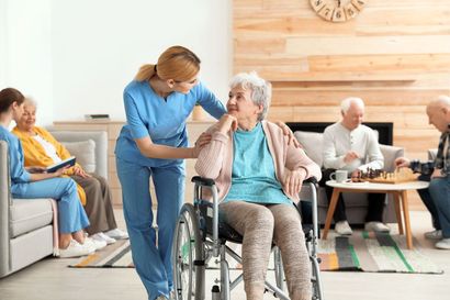 Caregiver helping a seated woman in a wheelchair in a bright nursing home common room Caregiver helping a seated woman in a wheelchair in a bright nursing home common room