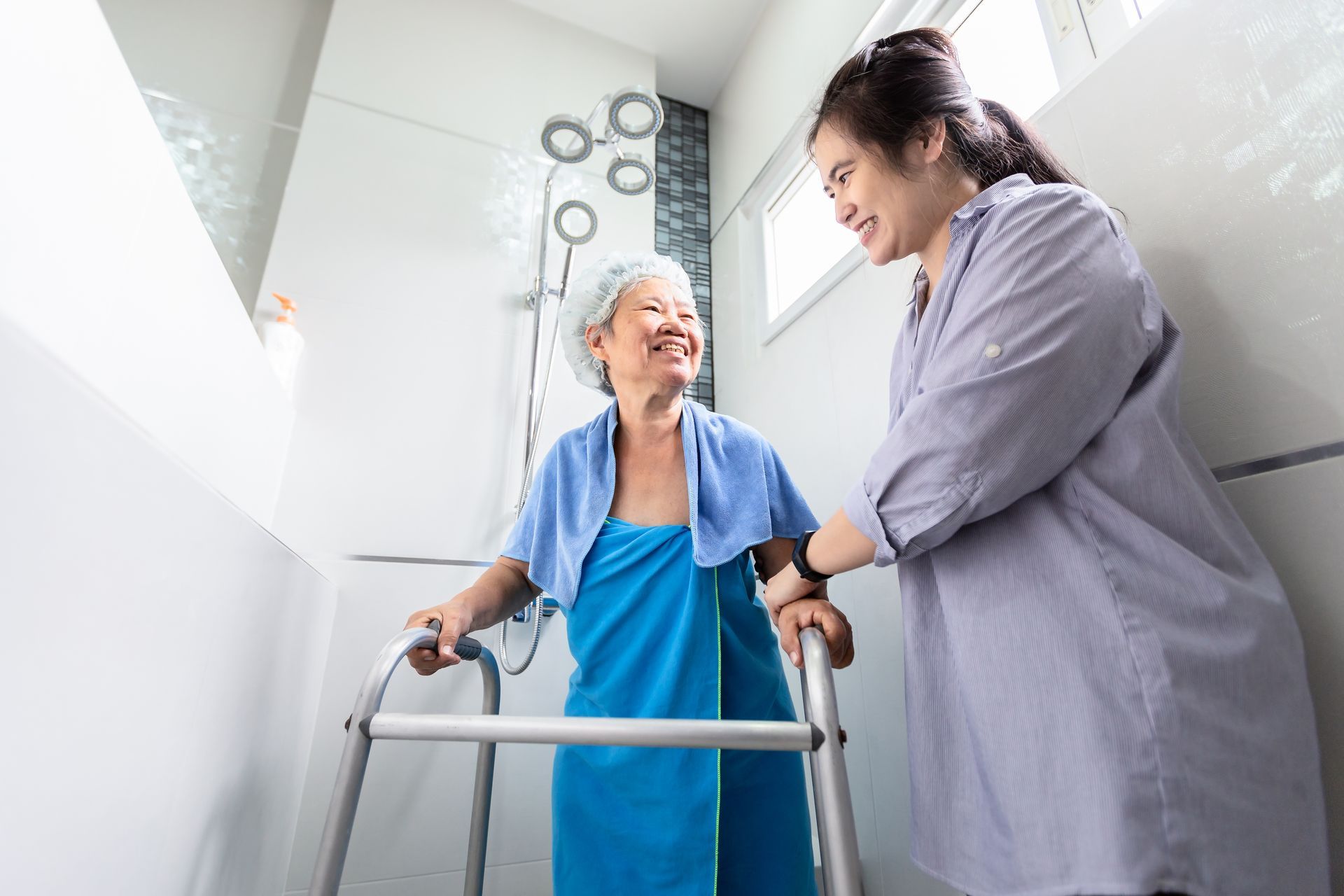 Caregiver helping an elderly patient with a walker in a bright bathroom Caregiver helping an elderly patient with a walker in a bright bathroom