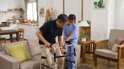 Person using a walker with caregiver support in a bright living room Person using a walker with caregiver support in a bright living room