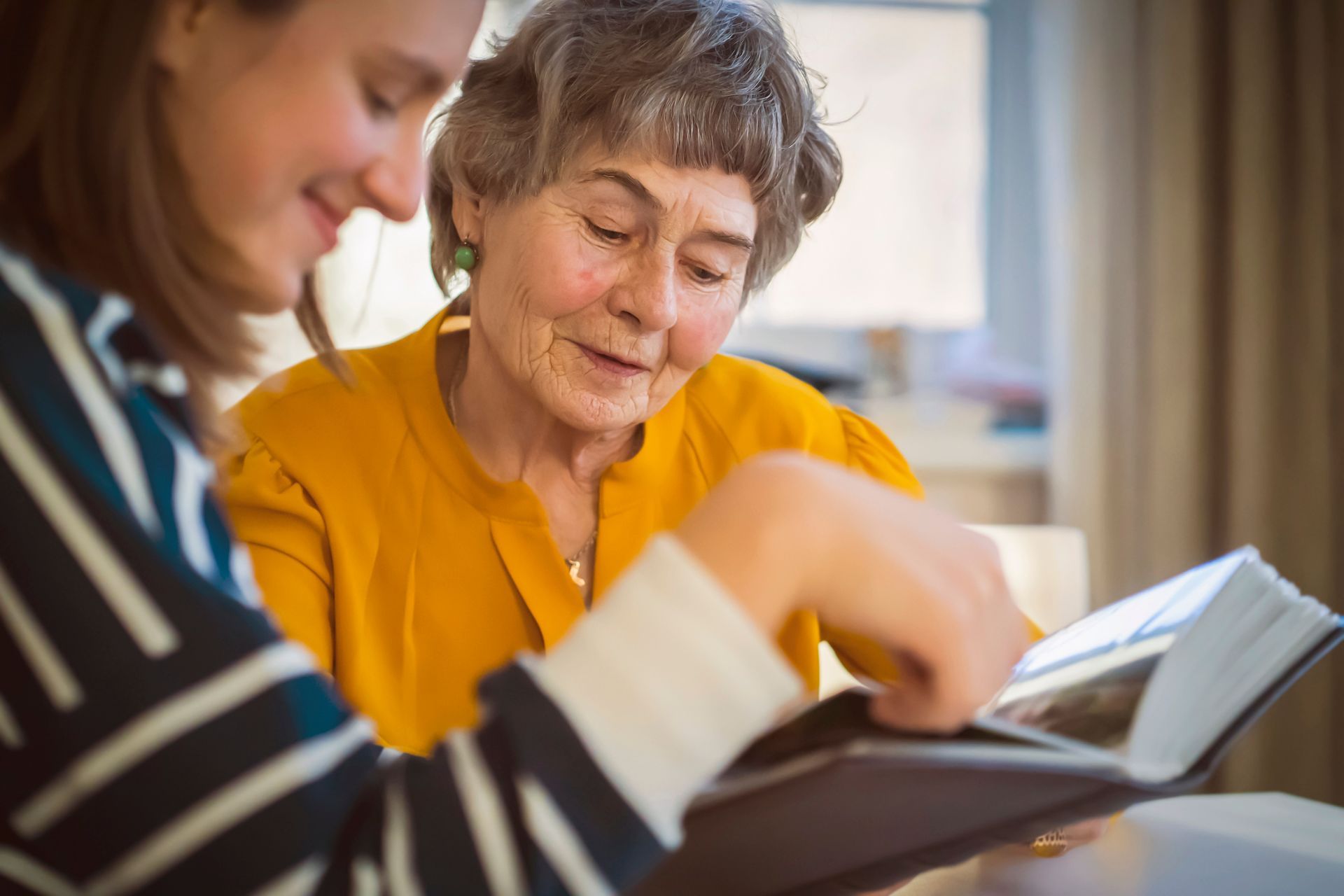 Two women reviewing an open book together at a table, one pointing to a page. Two women reviewing an open book together at a table, one pointing to a page.