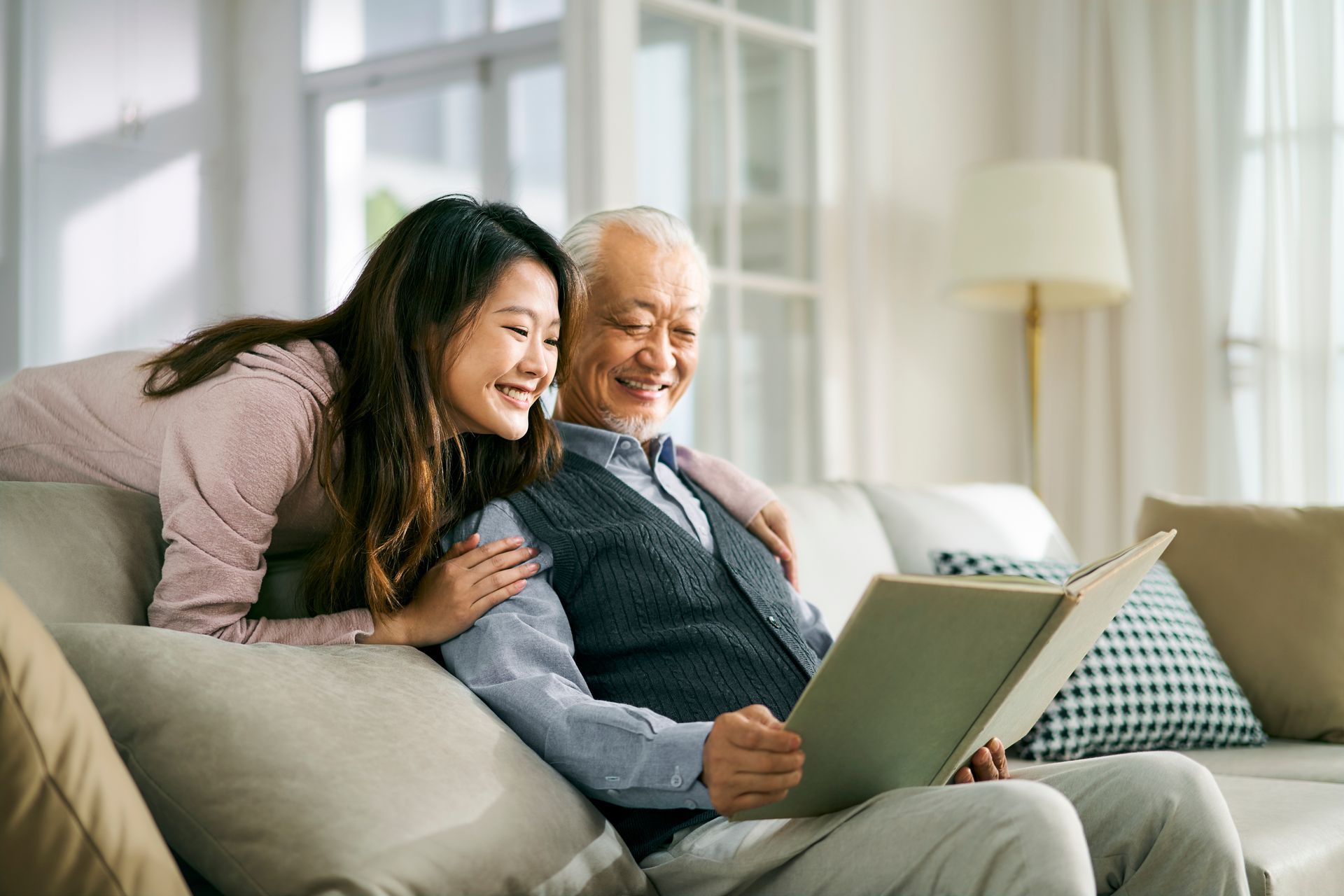 Two people smiling on a couch, looking at a laptop in a bright living room.