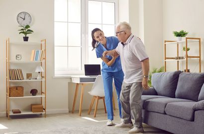 Older man and woman stretching in a bright living room beside a gray sofa and laptop table Older man and woman stretching in a bright living room beside a gray sofa and laptop table