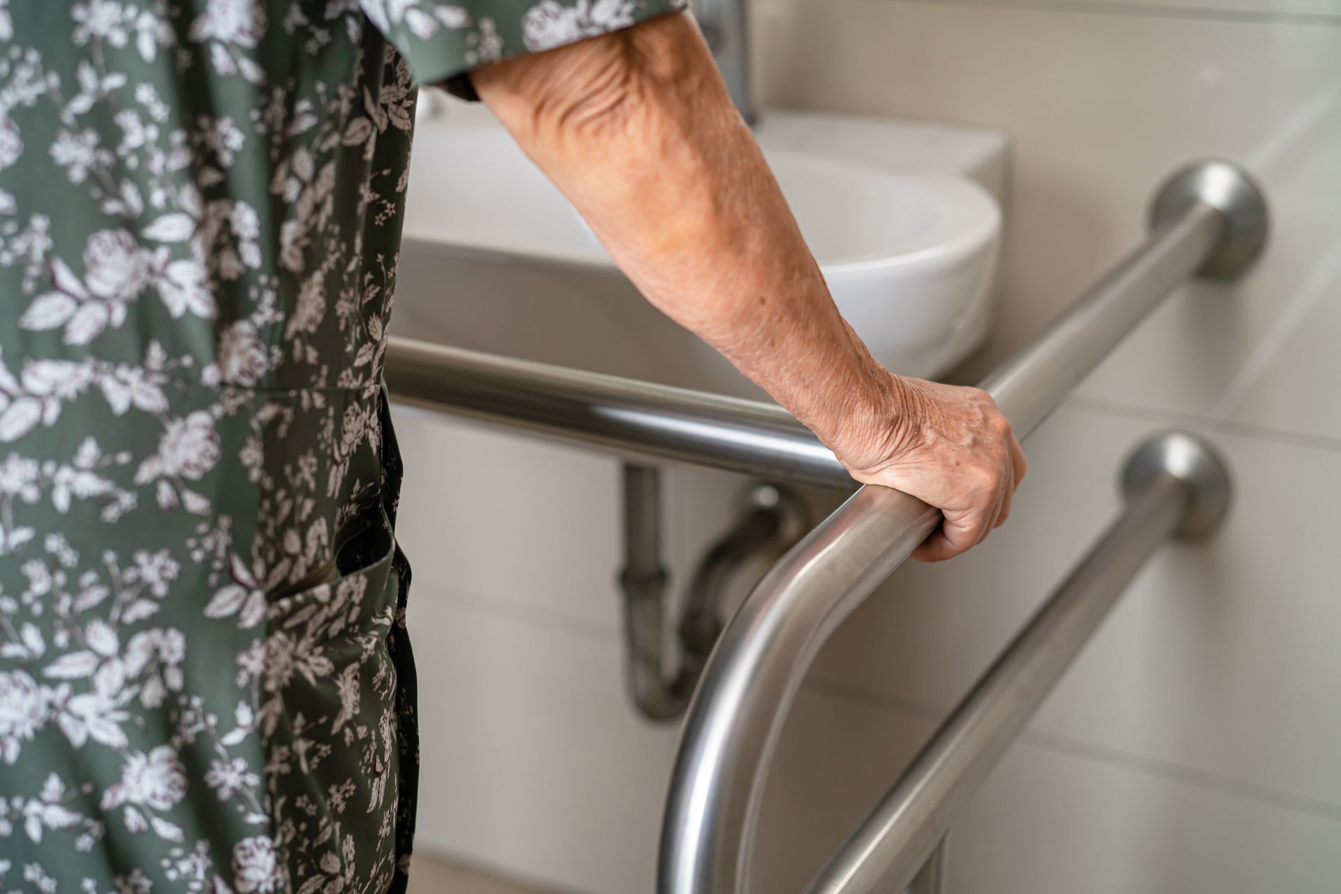 Person holding a bathroom grab bar near a sink for support