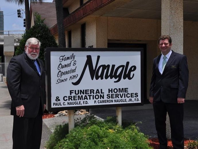 Two men posing in front of the Naugle Funeral Home and Cremation Services sign
