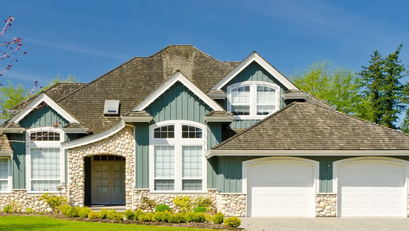 Large blue-gray suburban house with stone accents and a three-car garage on a sunny day
