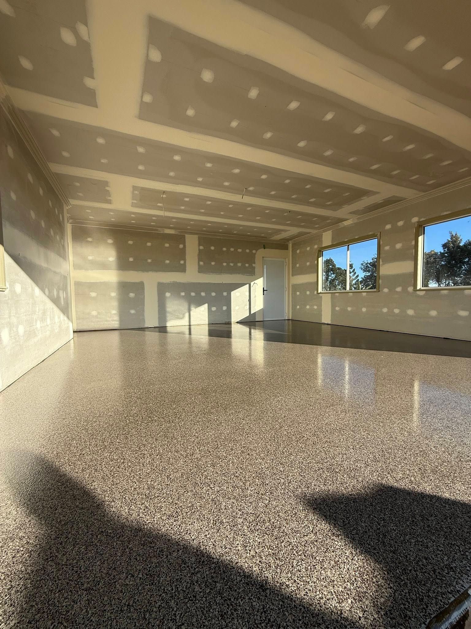 Empty Sunlit Room With Unfinished Drywall, Speckled Floor, and Windows Along One Wall — All Grind & Coat in Tablelands, QLD