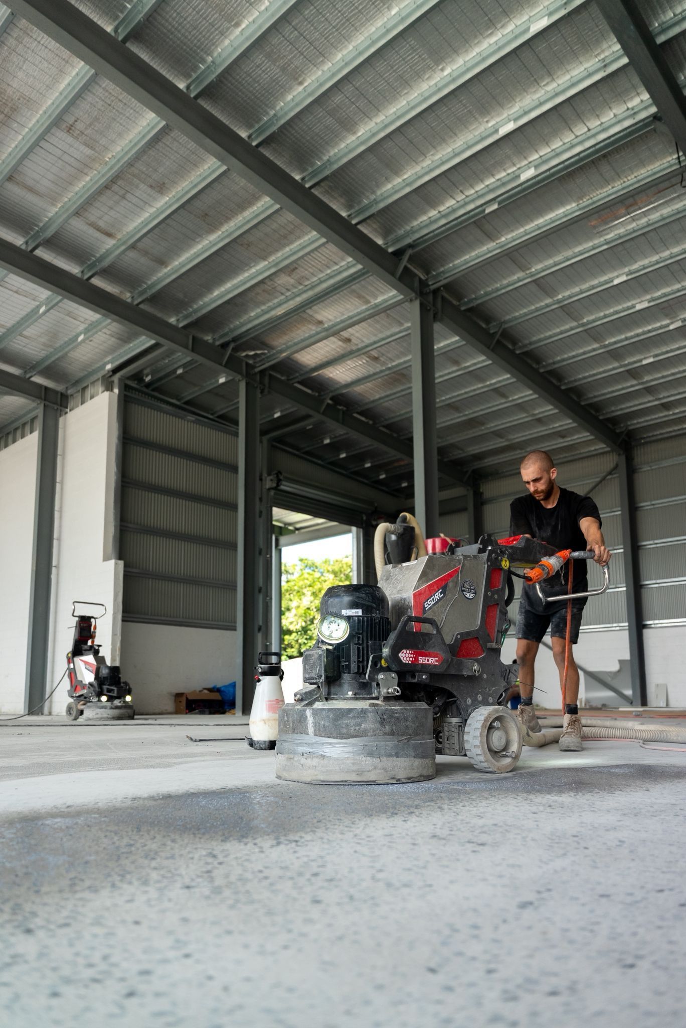Worker Operating a Floor Grinder Inside a Large Unfinished Metal Building — All Grind & Coat in Cairns, QLD
