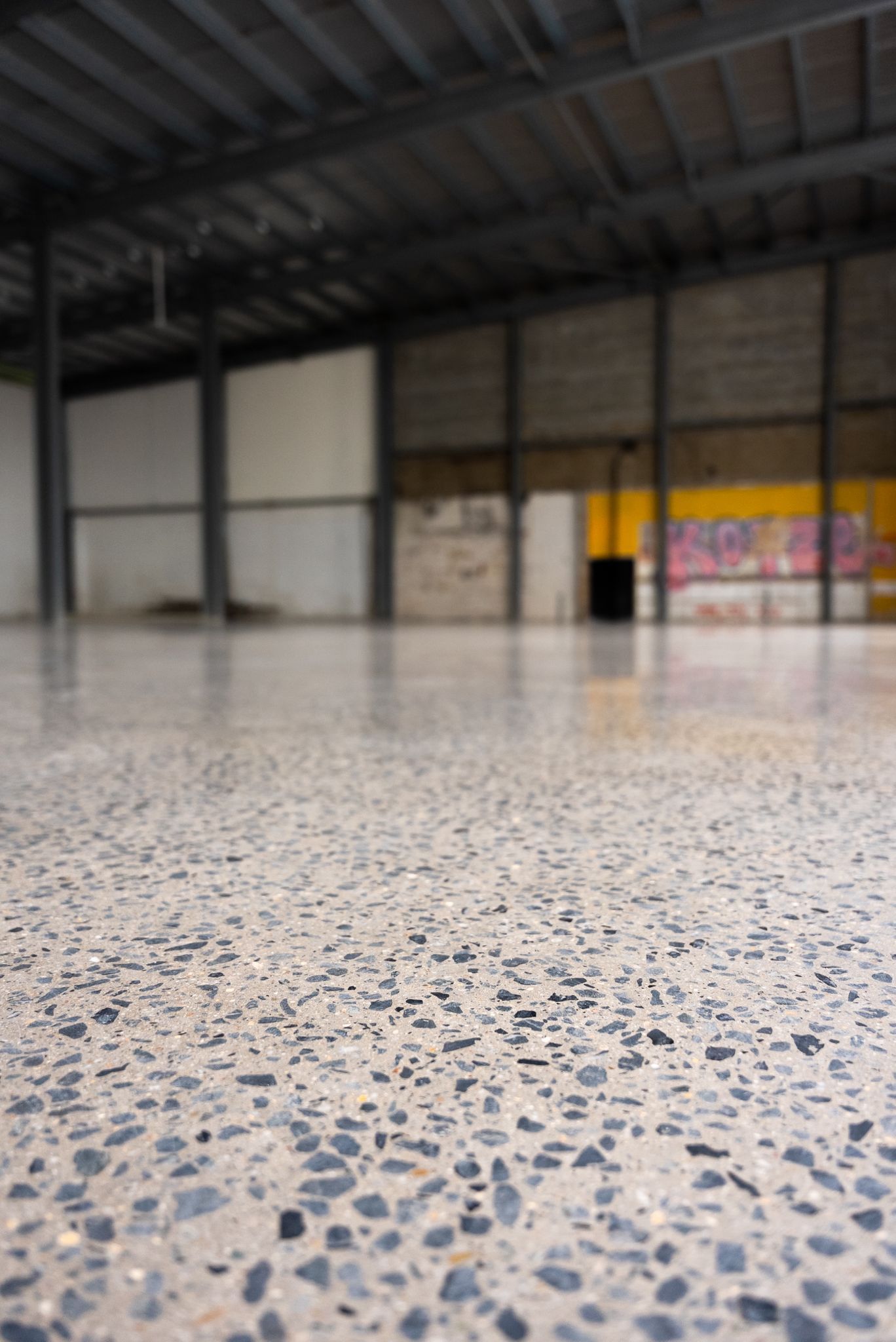Empty Warehouse Interior With Polished Speckled Concrete Floor and Metal Roof Beams — All Grind & Coat in Cairns, QLD