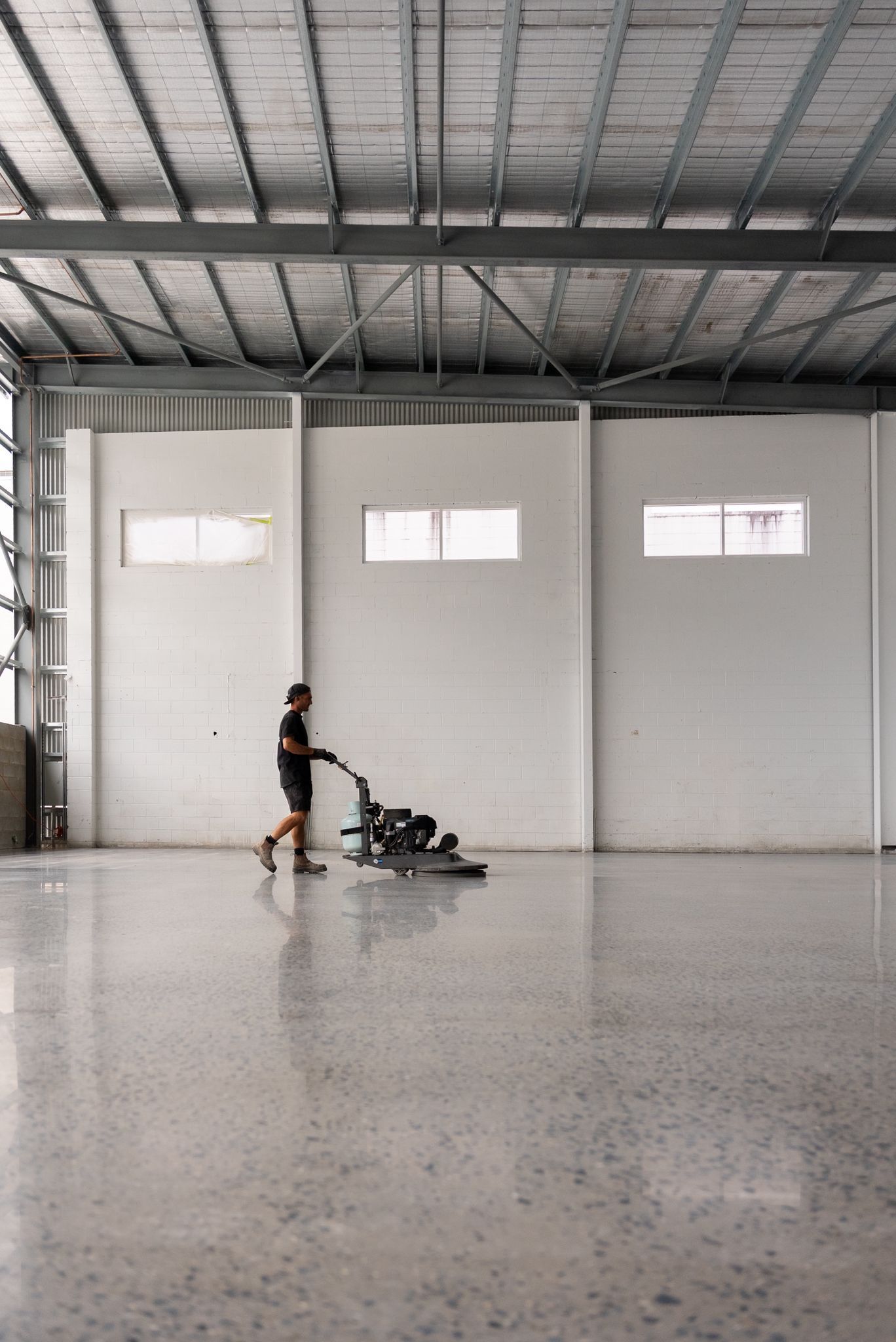 Person Operating a Floor Scrubber in a Large Empty Warehouse With a High Metal Ceiling — All Grind & Coat in Cairns, QLD