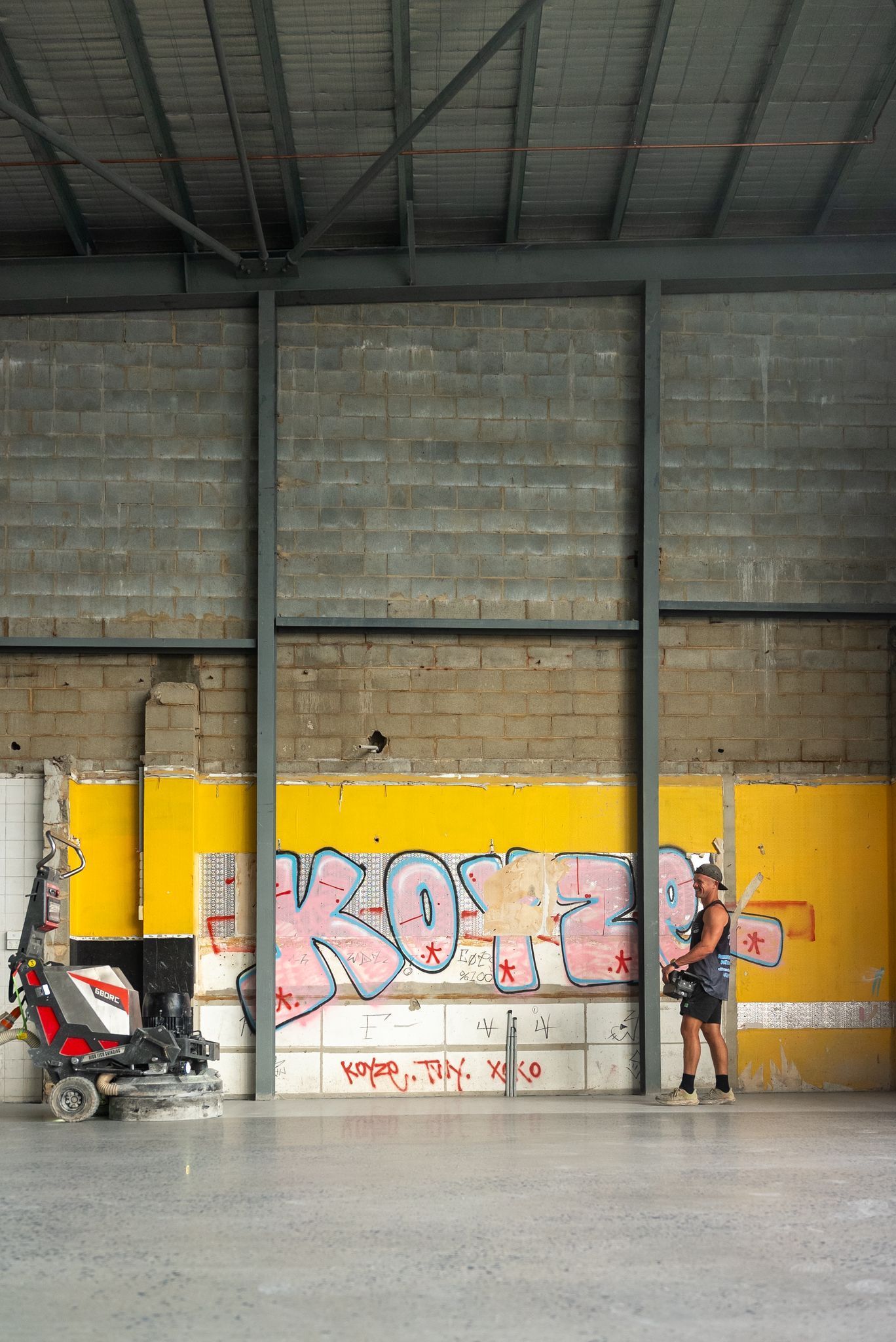 Two People Standing in an Industrial Garage With Yellow Walls and Colorful Graffiti — All Grind & Coat in Cairns, QLD