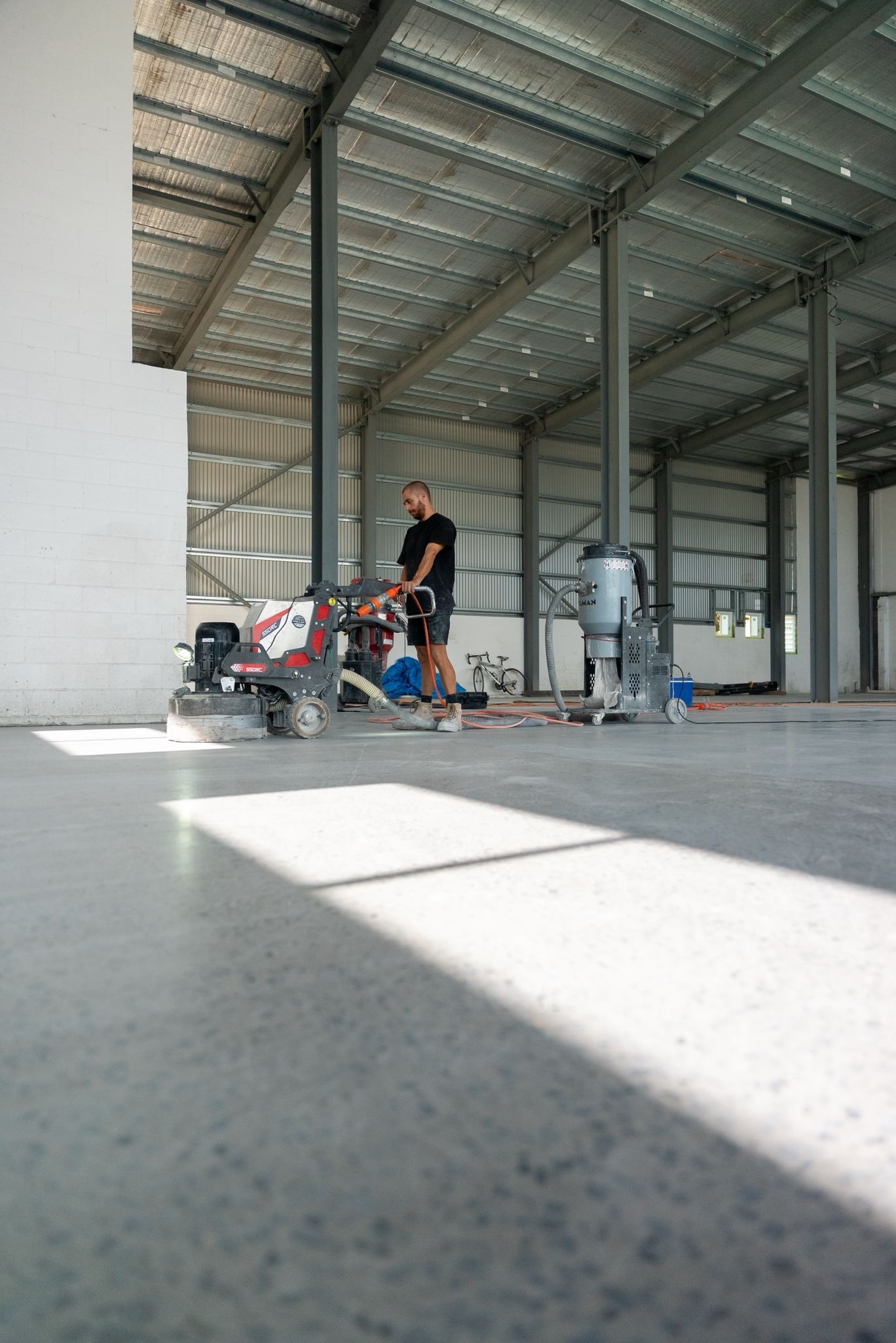People Working Near a Red Stroller in a Large Unfinished Warehouse-like Space — All Grind & Coat in Cairns, QLD
