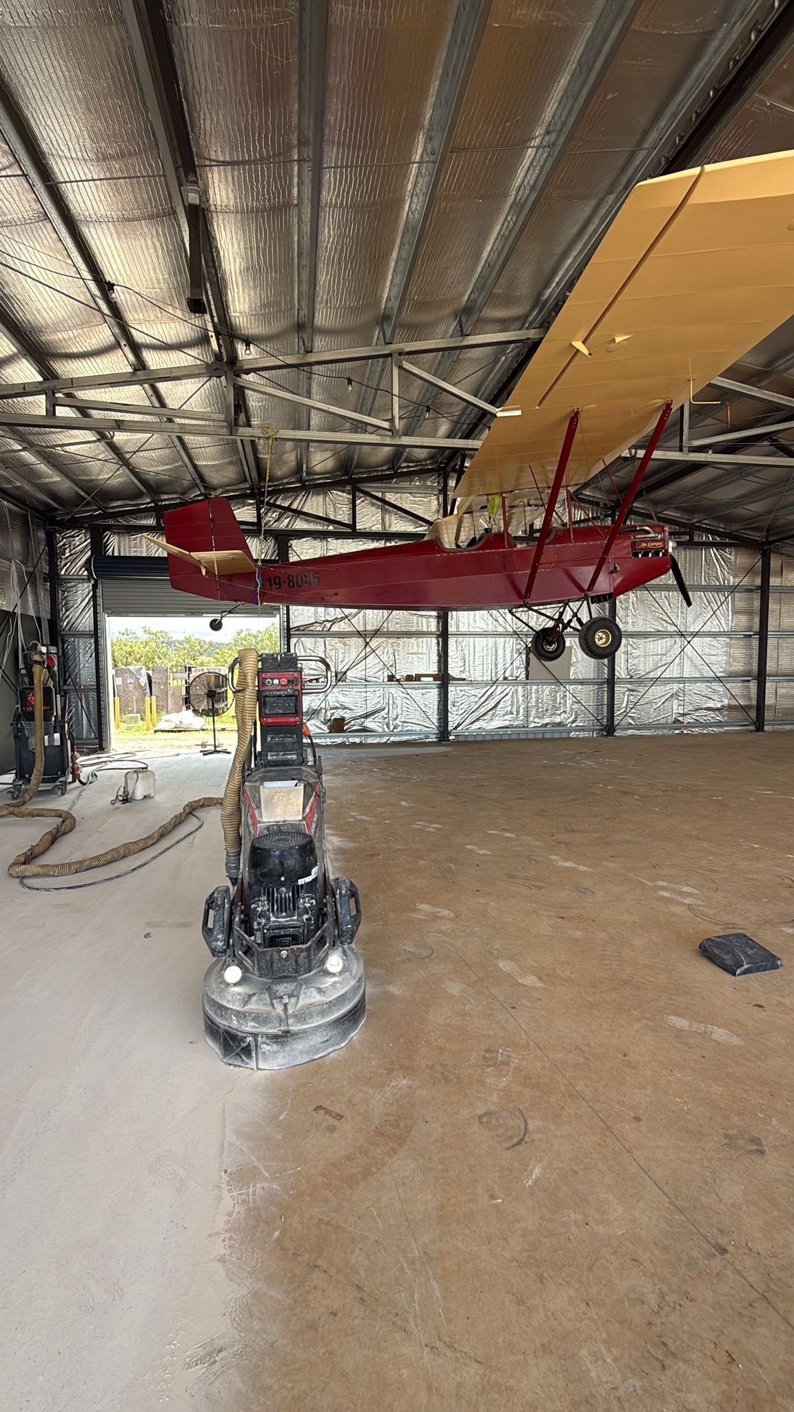 A Red Biplane Inside a Hangar With a Concrete Floor and Exposed Metal Ceiling — All Grind & Coat in Cairns, QLD