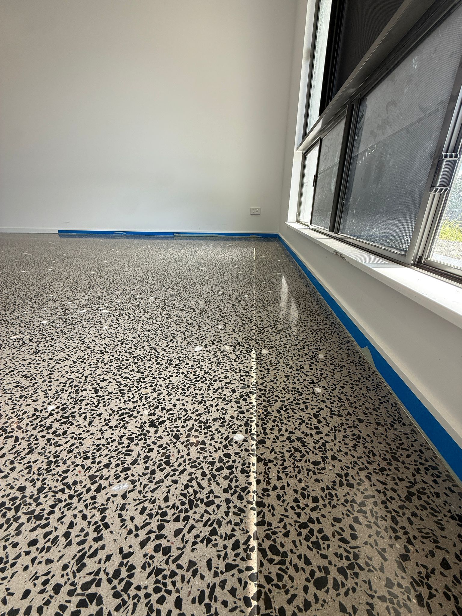 Empty Room With Speckled Floor, White Walls, and a Windowed Corner With Blue Painter’s Tape — All Grind & Coat in Cairns, QLD