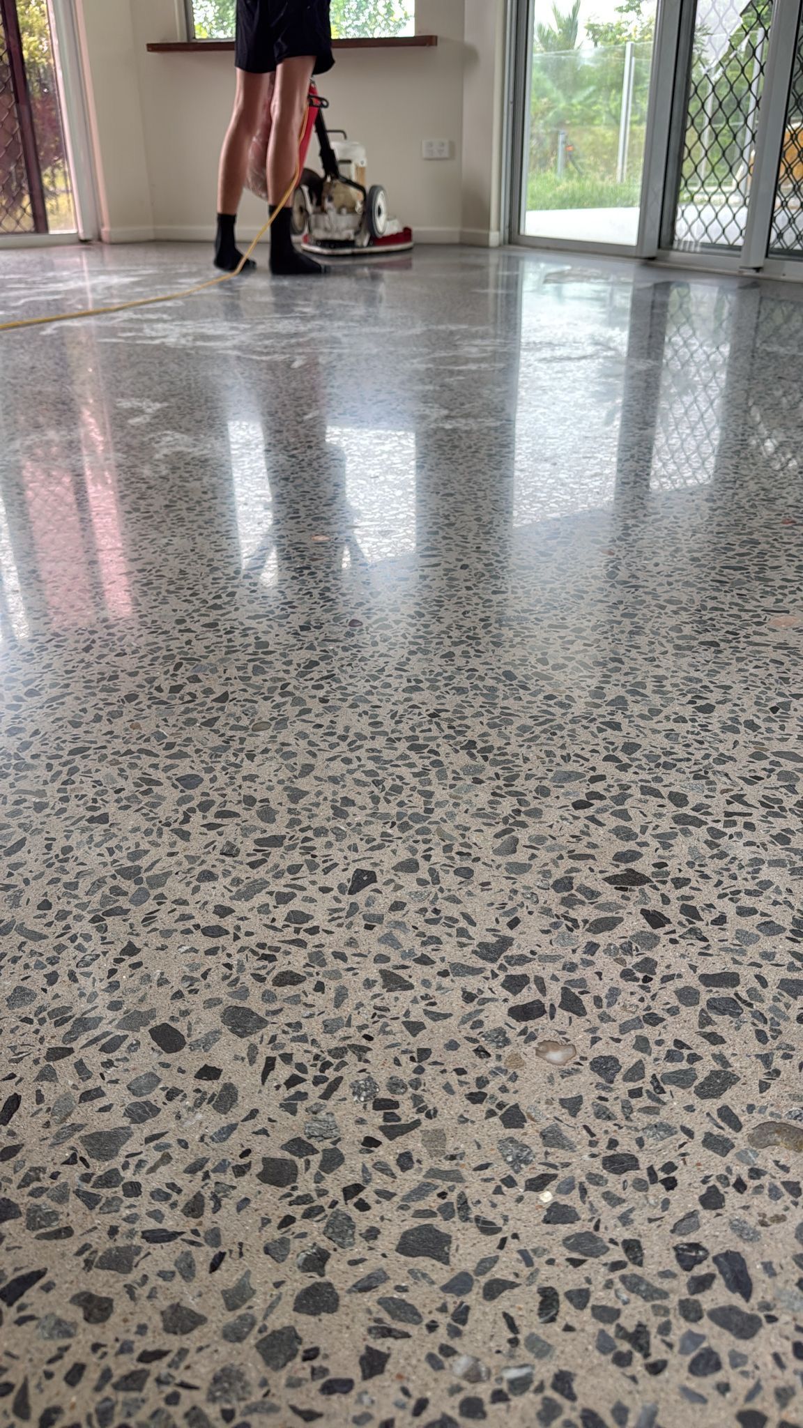Person Standing Indoors on a Speckled Terrazzo Floor Near a Red Walker by a Bright Window — All Grind & Coat in Cairns, QLD