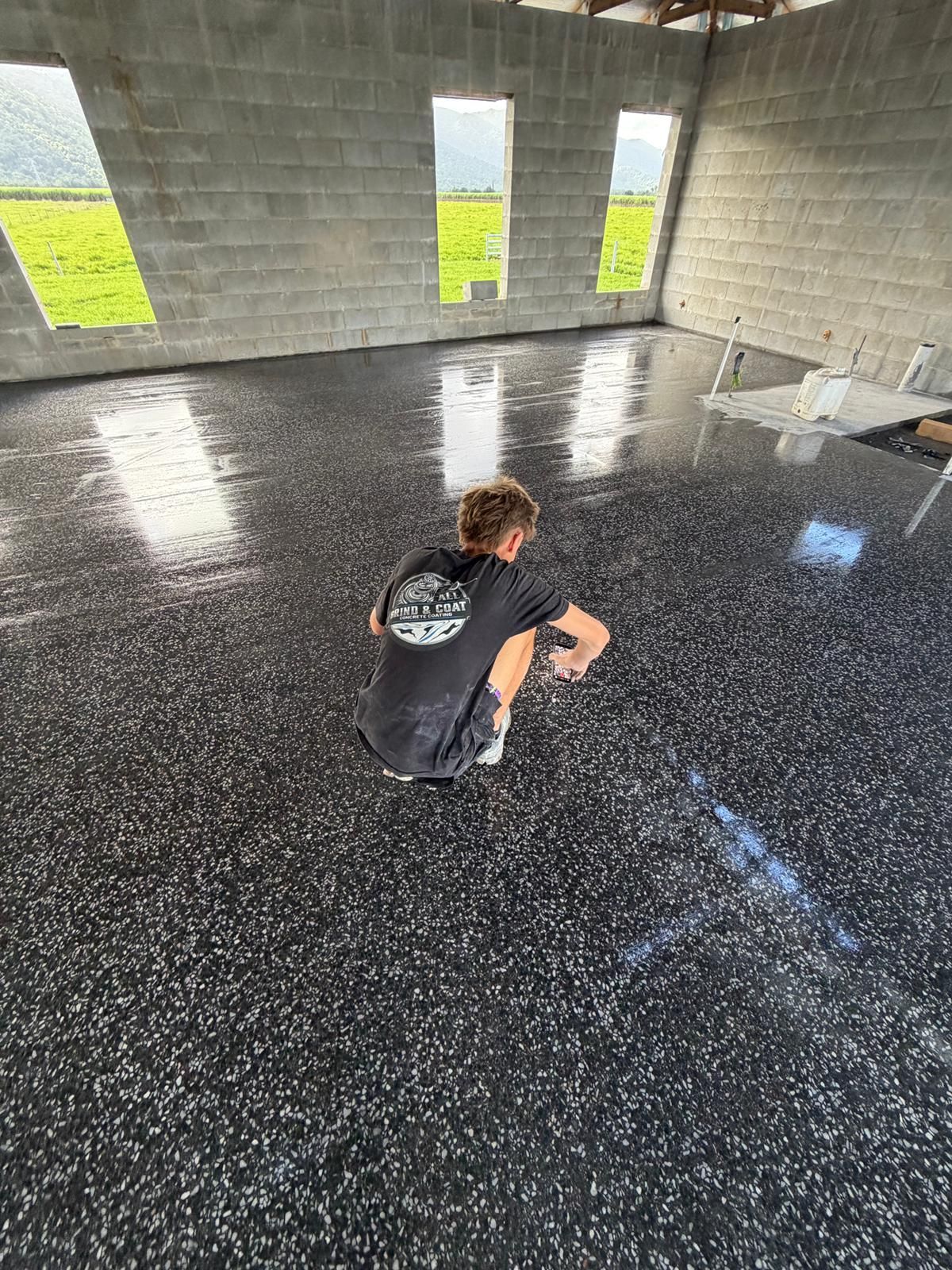 Person Crouching on a Glossy Black Floor Inside an Unfinished Concrete Room With Windows — All Grind & Coat in Cairns, QLD