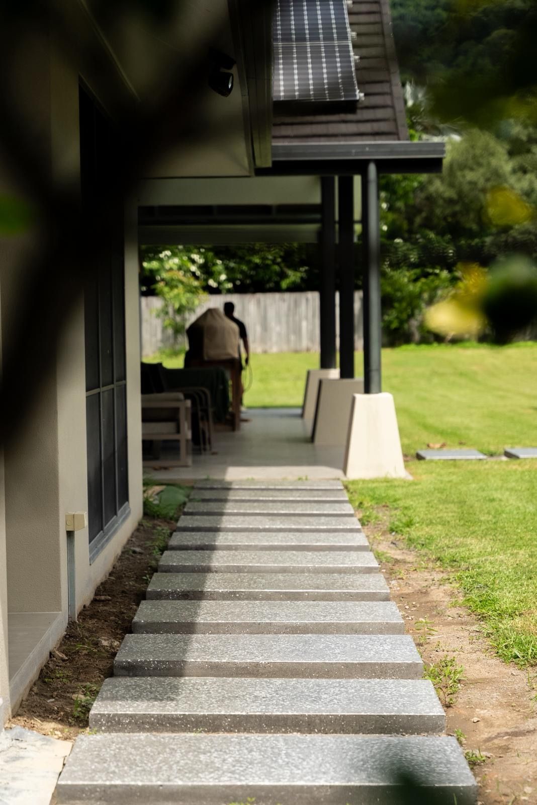 Covered Walkway With Stone Path Leading to a Seated Person Beside a Grassy Courtyard — All Grind & Coat in Cairns, QLD