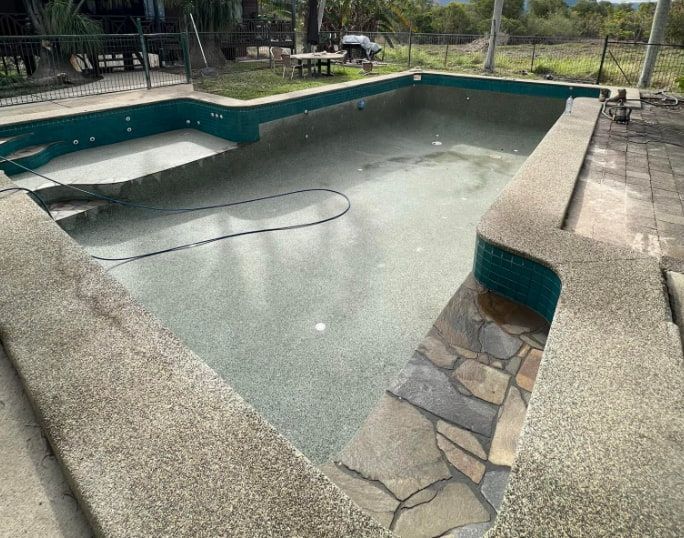 Empty Pool With a Mottled Grey Interior, Green Tiles, and Stone Edging — All Grind & Coat in Port Douglas, QLD