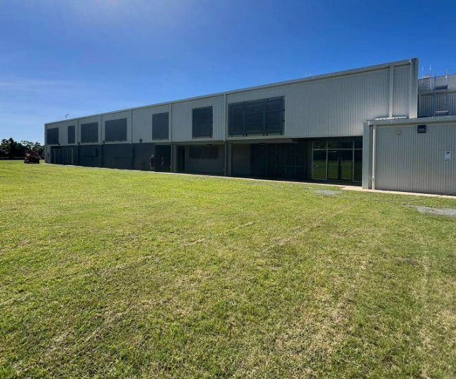A Large Building With a Lot of Windows is Sitting on Top of a Lush Green Field — All Grind & Coat in Cairns, QLD