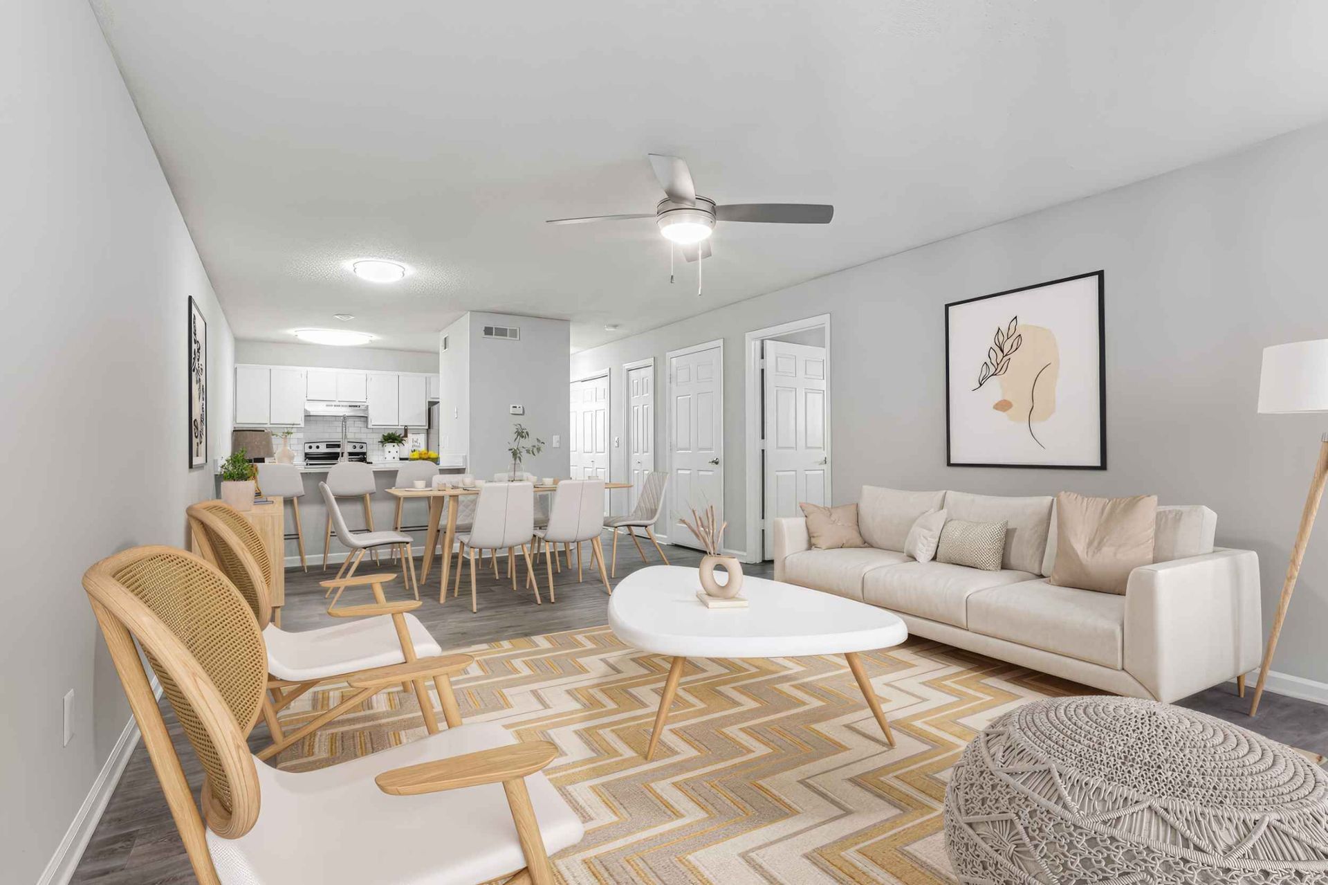 Bright open-concept living room with white sofa, patterned rug, round coffee table, and dining area in back