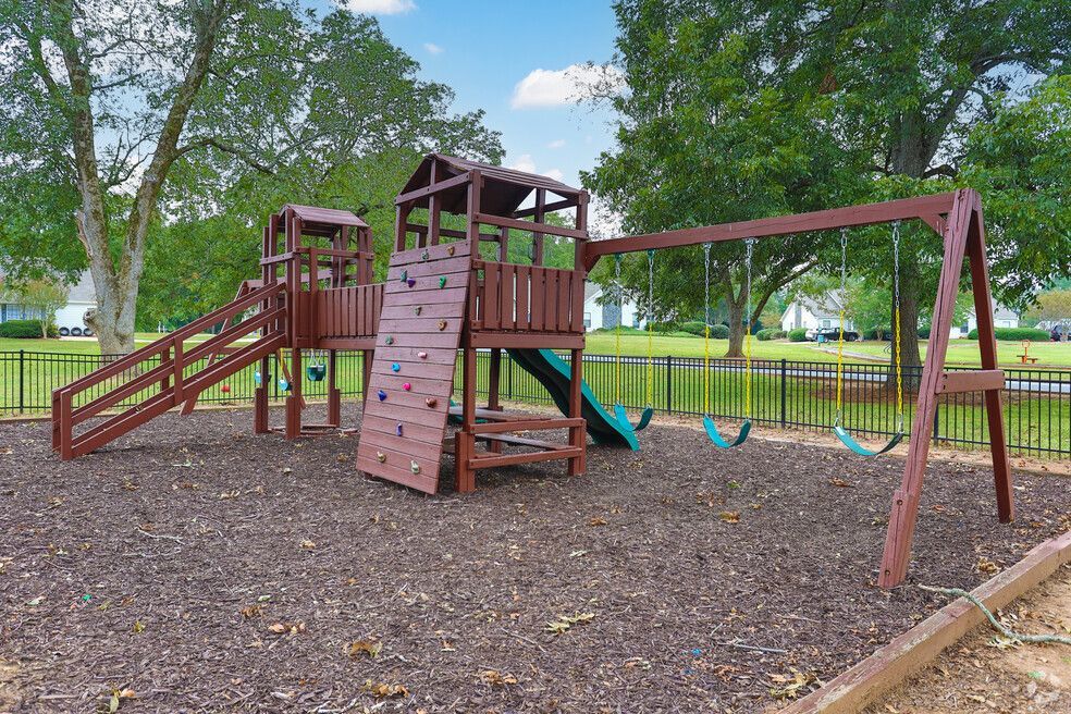Wooden playground with slides, climbing wall, swings, and trees in a park