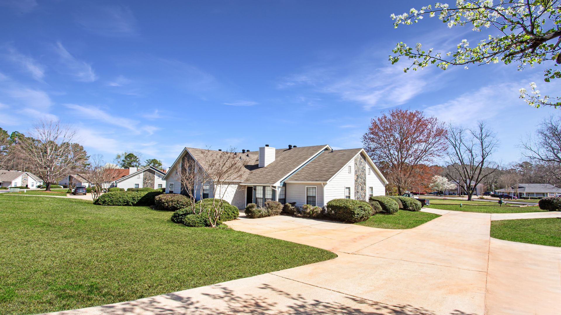 Suburban brick house with large lawn and driveway under a bright blue sky.