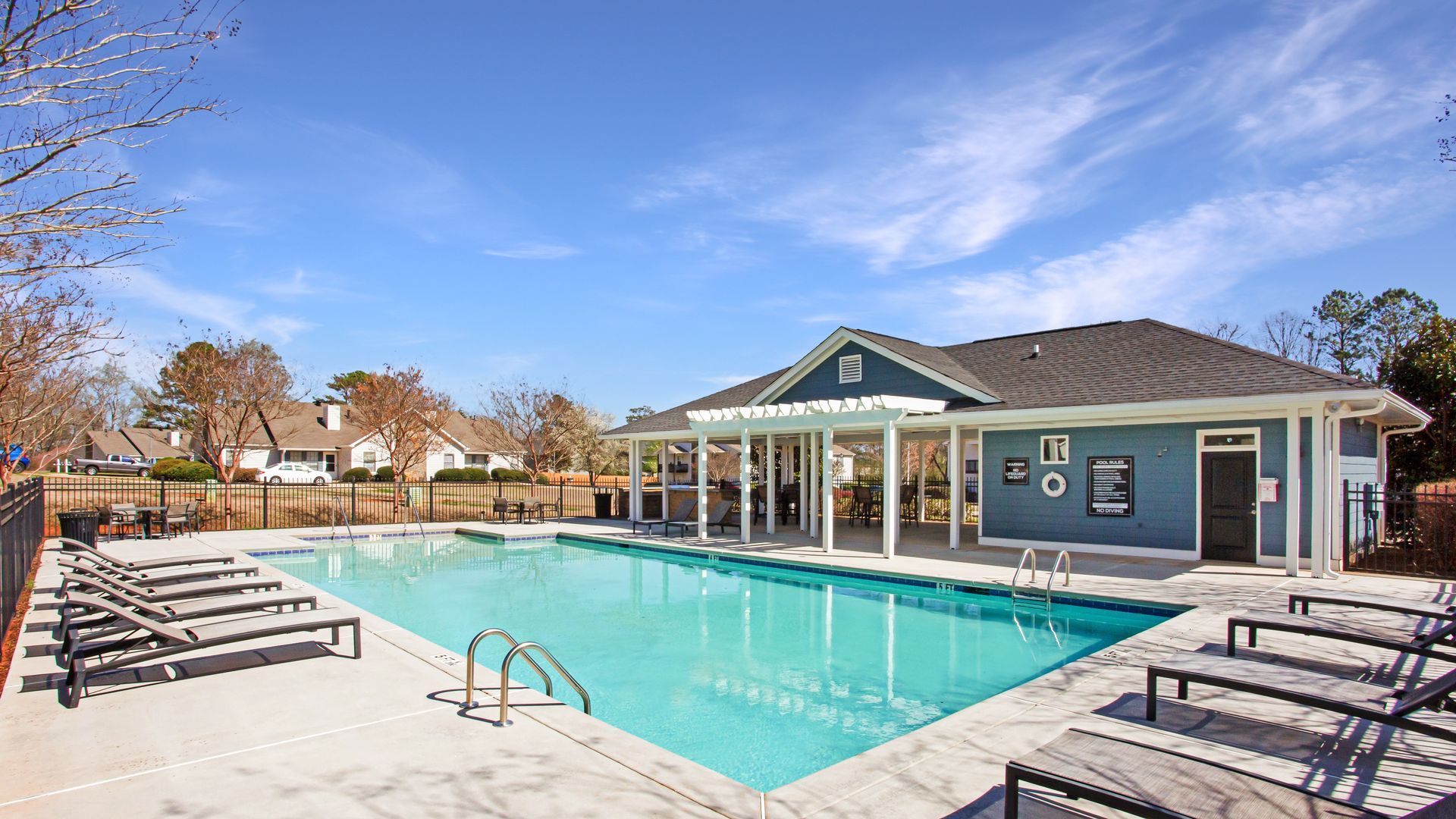Outdoor swimming pool with lounge chairs and a clubhouse under a blue sky