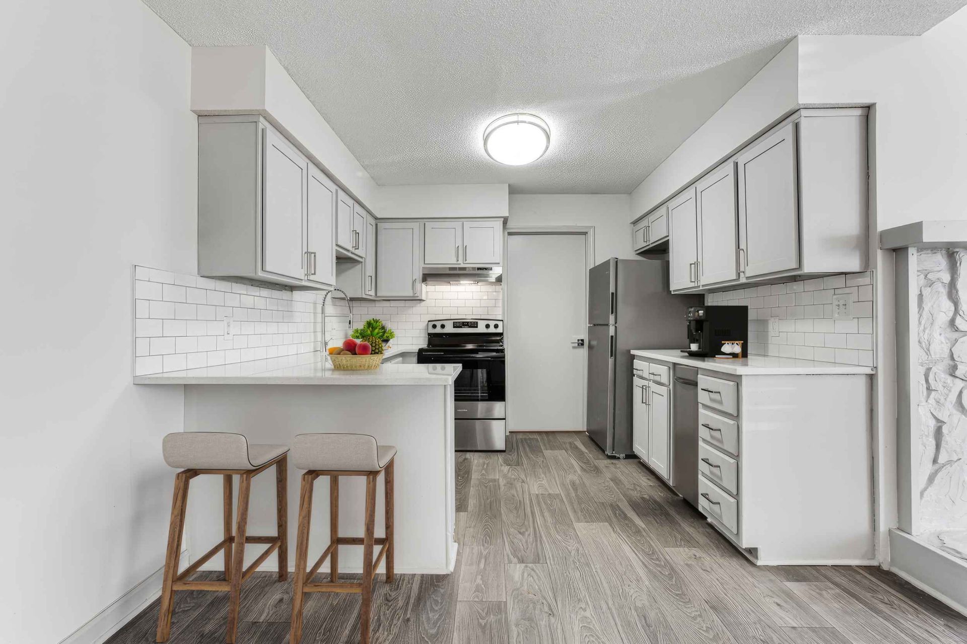 Bright white kitchen with gray flooring, island stools, stainless appliances, and a ceiling light