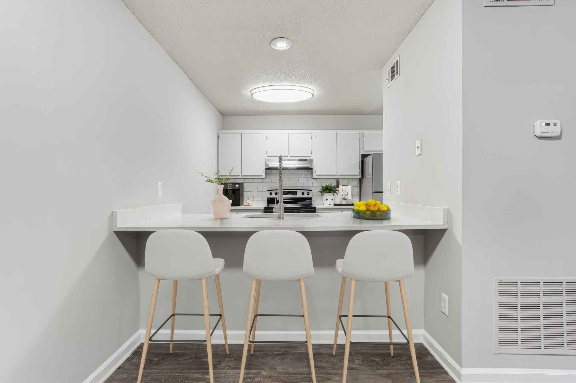 Bright modern kitchen pass-through with three white bar stools and a fruit bowl on the counter.