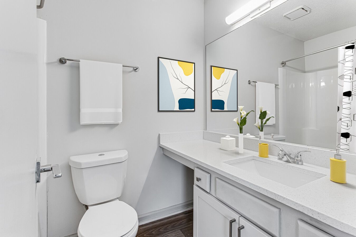 Bright white bathroom with toilet, vanity sink, large mirror, and framed wall art