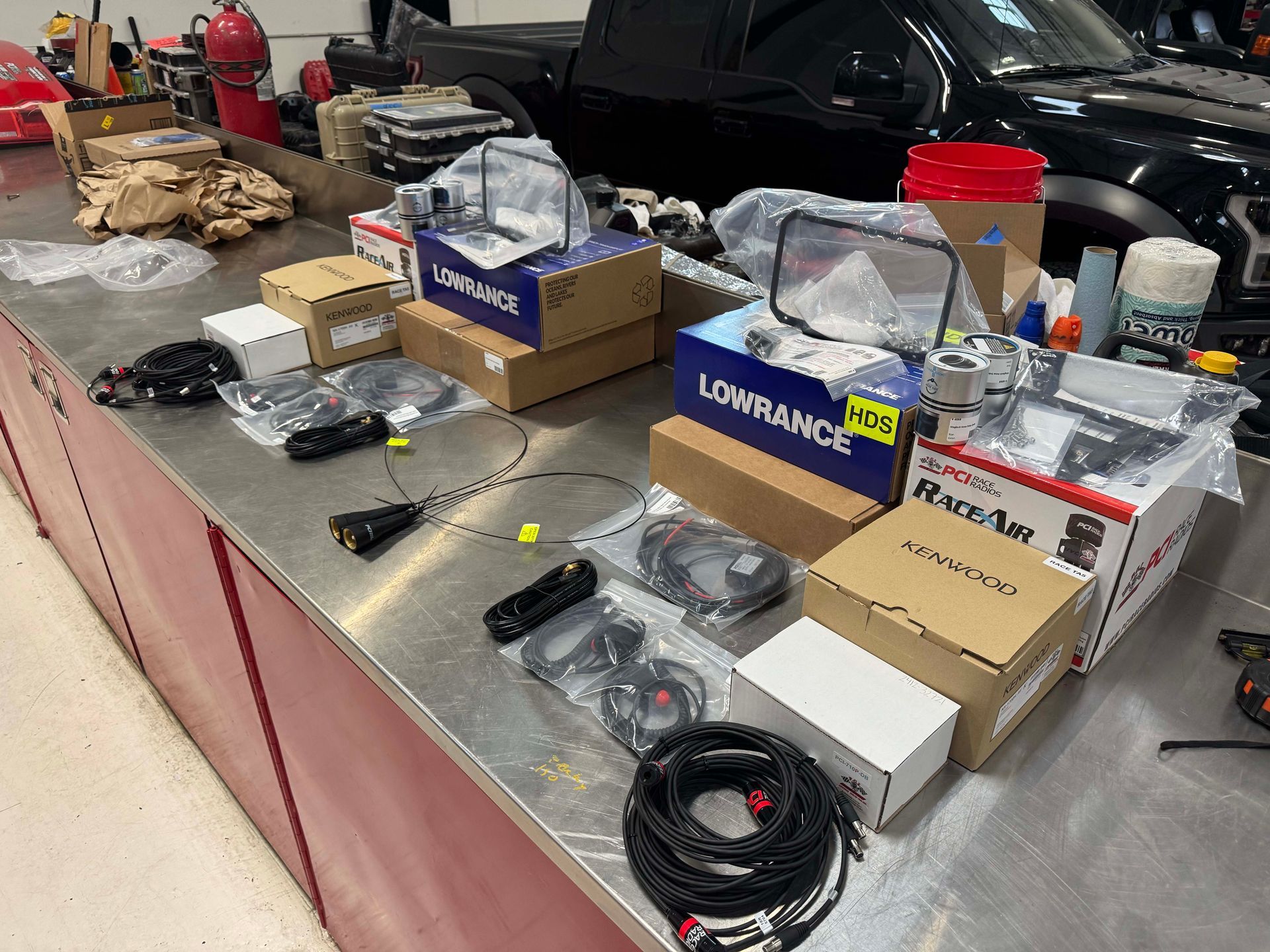 Assorted electronics and tools displayed on a table at a market or garage sale, with boxes and cables.