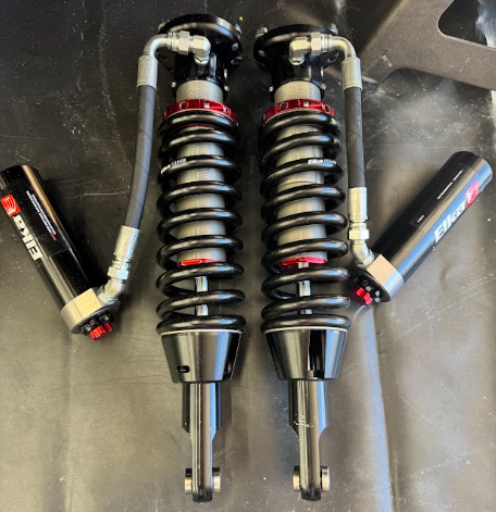 Pair of black coilover shock absorbers with remote reservoirs on a dark surface