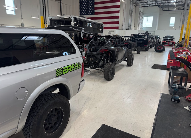 Off-road vehicles and trucks inside a garage, with an American flag on the wall.