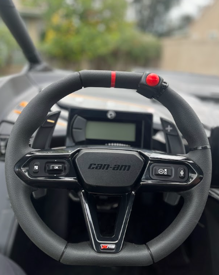 Can-Am steering wheel and dashboard inside a vehicle, with black trim and red accents