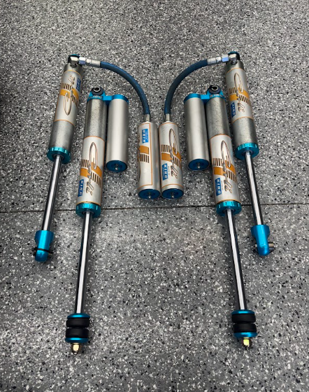 Two silver and blue car shock absorbers with hoses, laid out symmetrically on a gray surface.