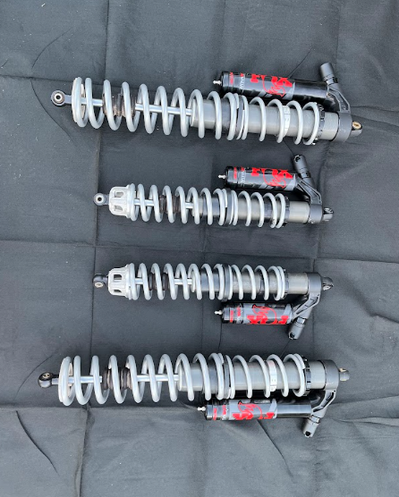 Four silver motorcycle shocks with red accents arranged vertically on a gray surface