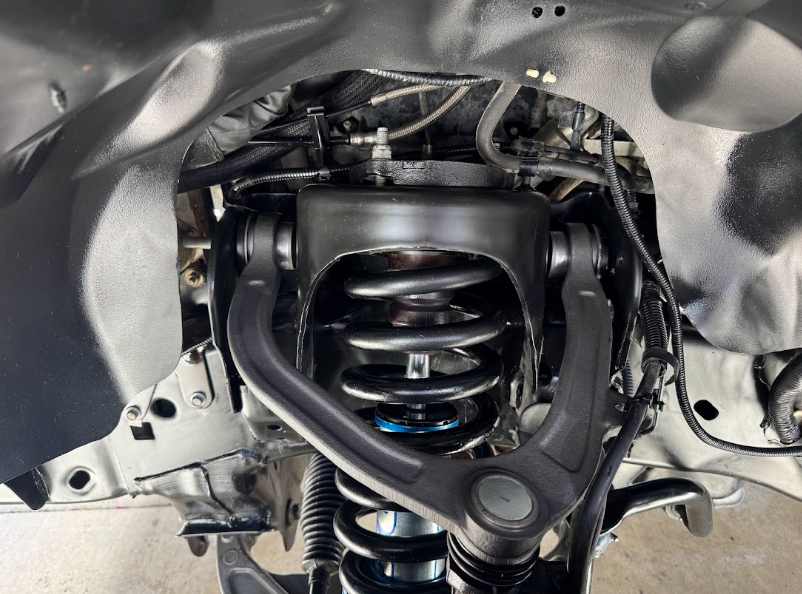 Car suspension coil spring and control arms under the wheel well, with metal body panels exposed