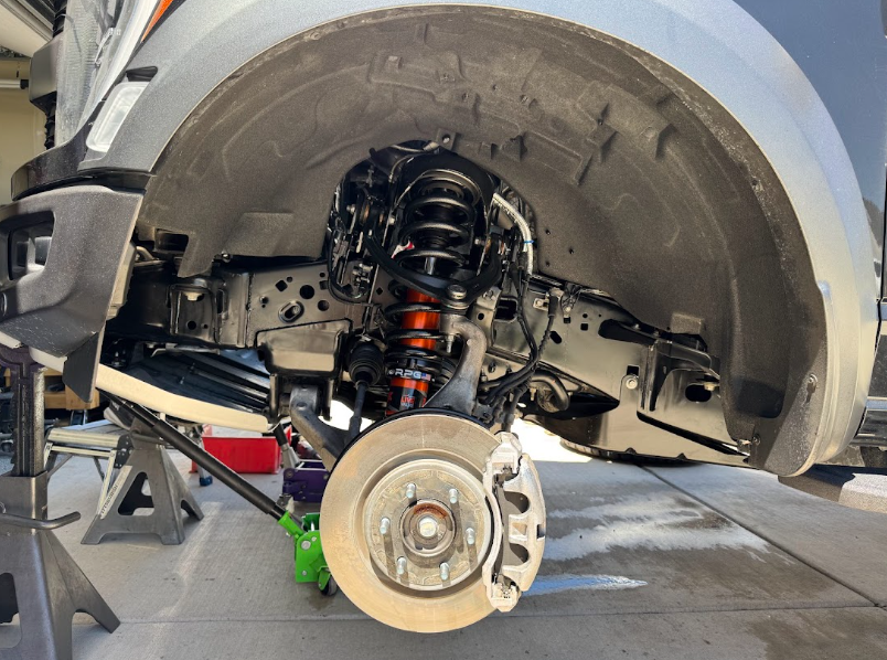 Car wheel removed, exposing brake rotor and suspension inside the wheel well at a repair shop