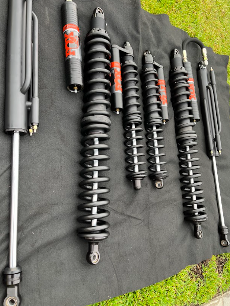Several black and gray motorcycle shocks and suspension components laid out on dark fabric.