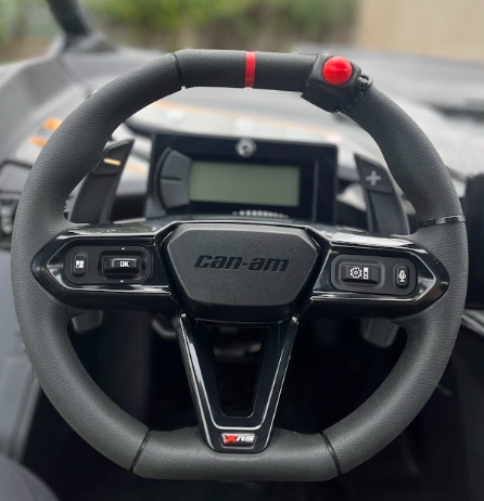 Can-Am steering wheel with dashboard display, black and red accents, in a vehicle cockpit
