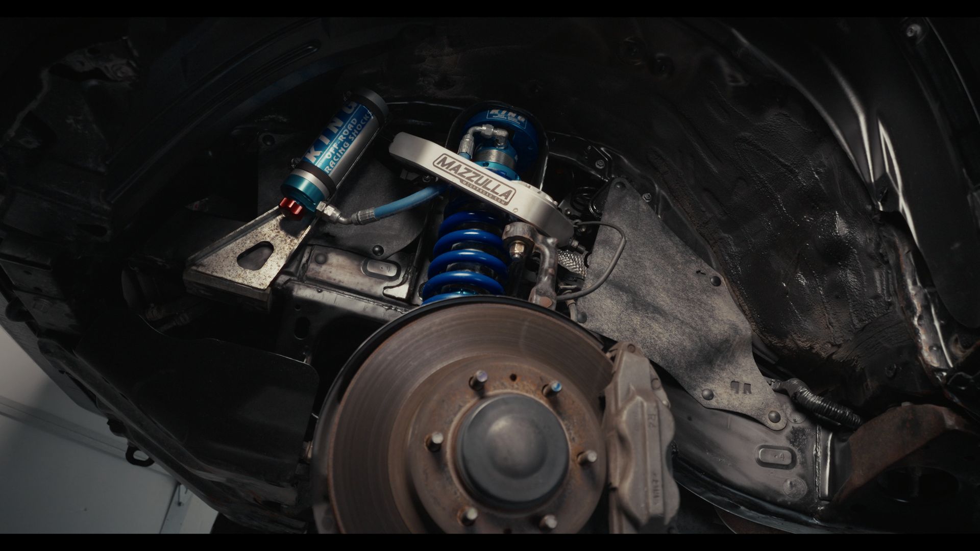 Close-up of a car’s front wheel and blue suspension components inside a dark wheel well.