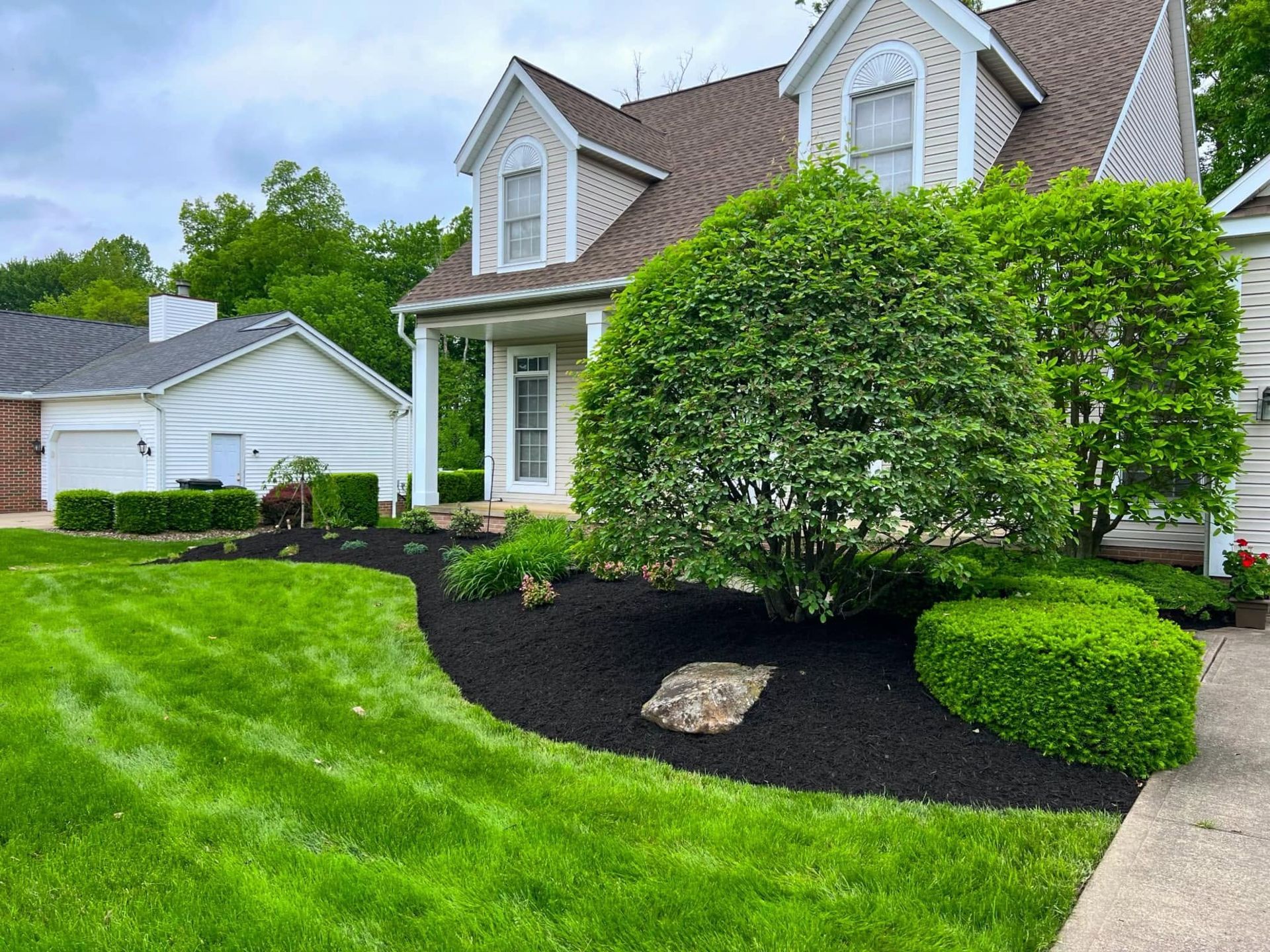 Suburban house with manicured lawn, shrubs, and black mulch landscaping by a driveway