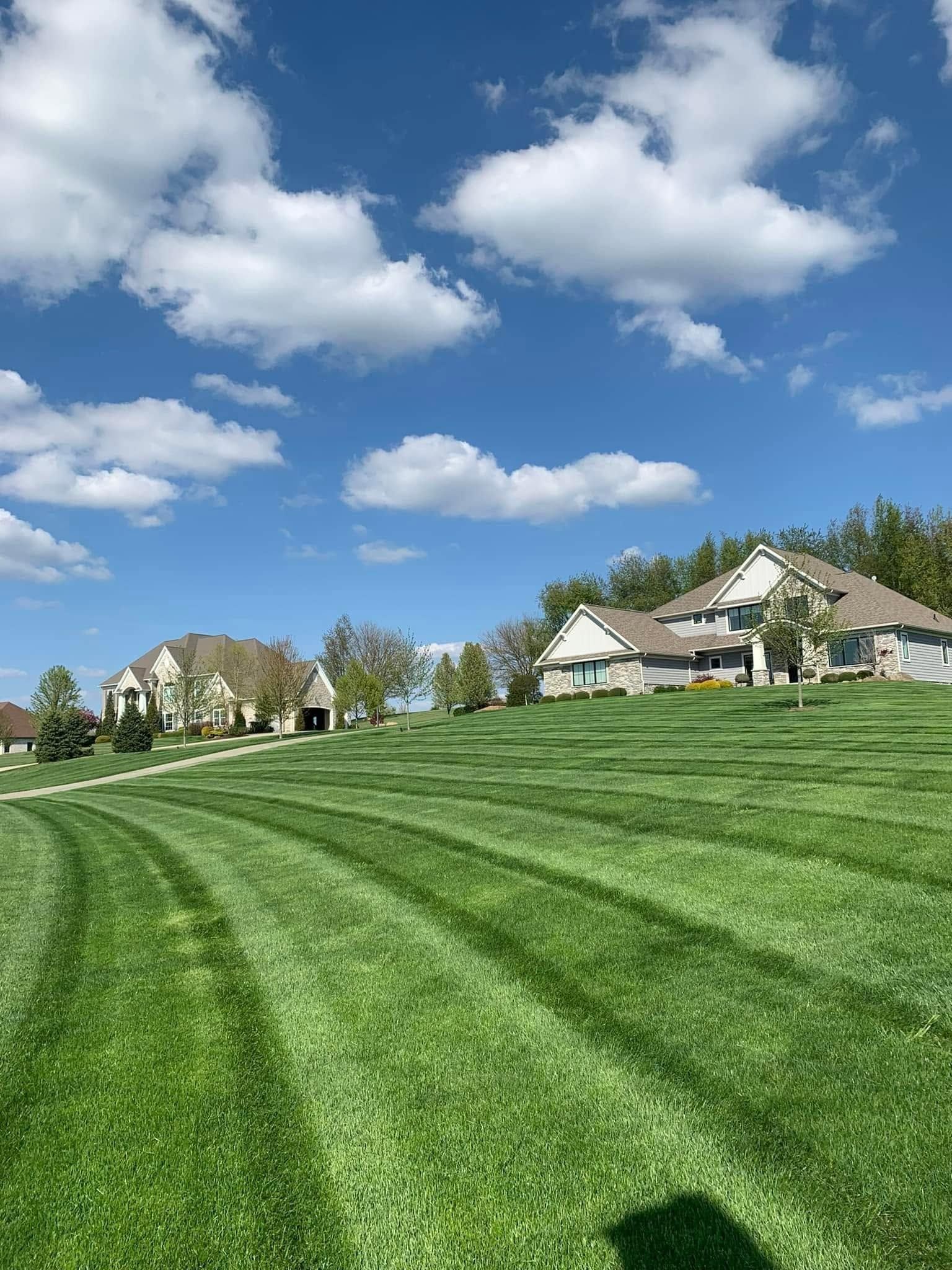 Green lawn with mower stripes beside suburban houses under a blue sky with scattered clouds