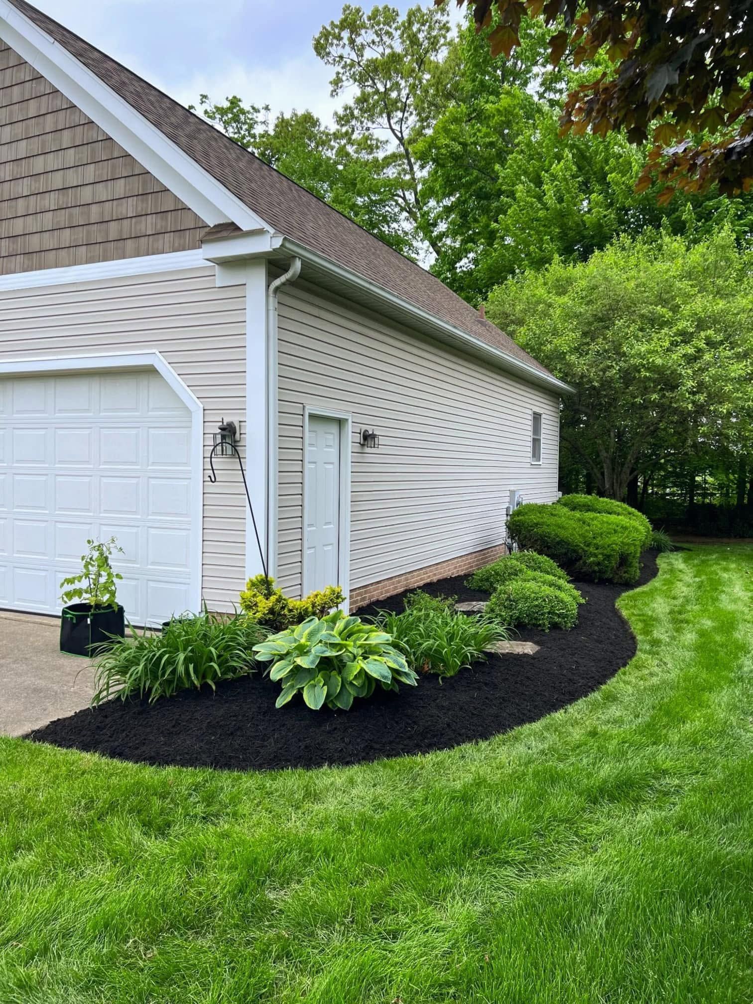 Suburban house exterior with white siding, garage, and curved mulch beds with shrubs and lawn