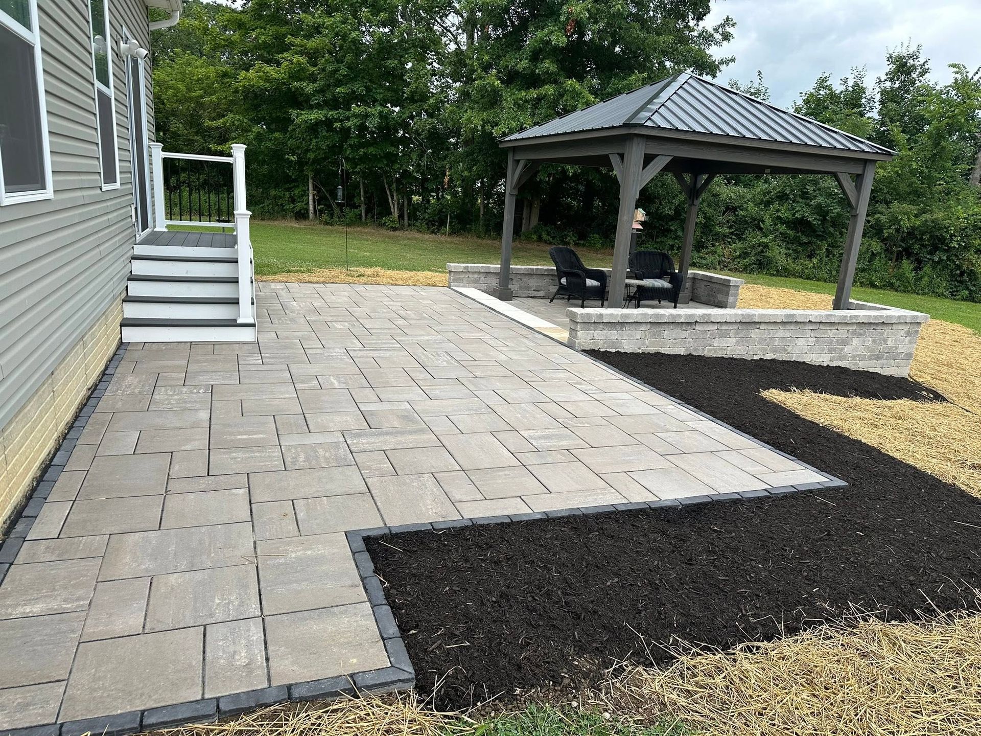 Backyard patio with gray pavers, a gazebo, and fresh black mulch along the edge