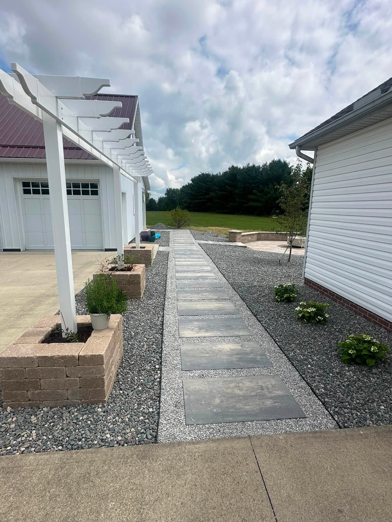 Stone walkway beside white houses and a gravel yard under a cloudy sky.