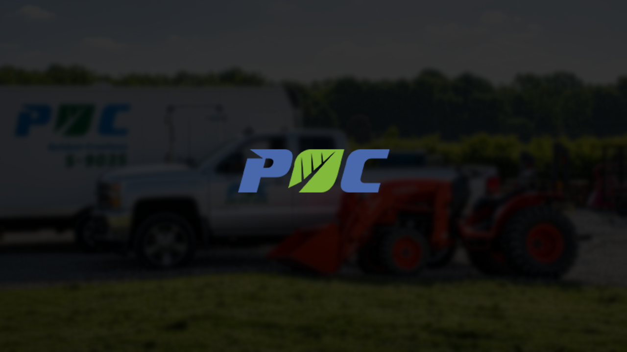 PMC logo over a red tractor parked beside a truck in a field