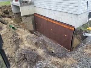 Panneau de drainage brun à fossettes installé contre une fondation en béton lors de l'excavation pour l'imperméabilisation.