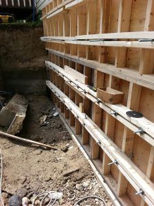 Coffrages en bois pour un mur de soutènement en cours de construction à côté d'une zone excavée.